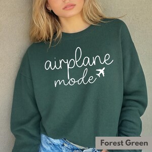 Op de afbeelding: Groen sweatshirt met de tekst "vliegtuigmodus" in witte letters en een klein vliegtuigpictogram.