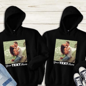 May include: Two black hoodies with a photo of a couple kissing on the front. The text "Your Text Here" is printed below the photo.