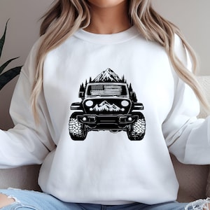 May include: White sweatshirt featuring a black graphic of a Jeep driving through a mountain landscape with an American flag on the front of the Jeep.