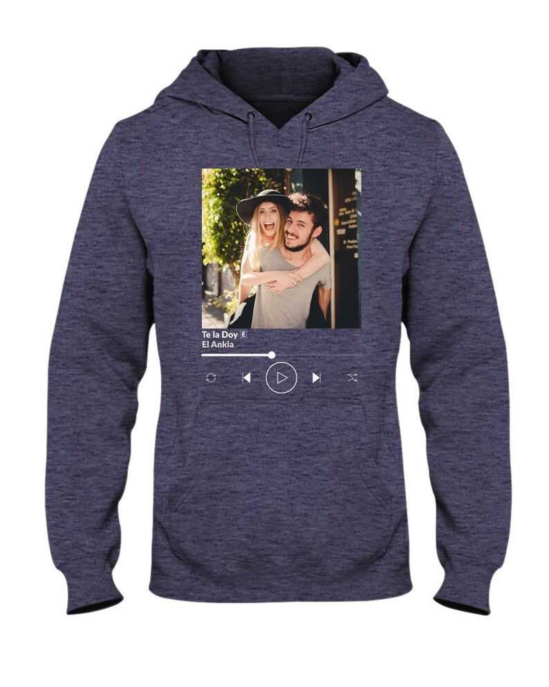May include: A navy blue hoodie with a photo of a couple on the front. The photo is in a white frame with a music player interface below it. The music player interface shows the song title "Te la Doy" by "El Ankla" and play, rewind, and fast forward buttons.