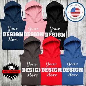 May include: Six different color hooded sweatshirts with the text "Your Design Here" printed in white on the front. The sweatshirts are arranged in a semi-circle on a woodgrain background.