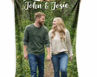 May include: A personalised blanket displaying a photograph of a couple in a forest, with the text "John & Josie" in white script. The blanket shows the couple walking in a natural setting, surrounded by green foliage.