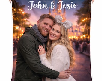 May include: A personalised fleece blanket displaying a couple embracing, with the text "John & Josie" in white script. The background shows a blurred image of a lit-up building and trees, creating a warm, romantic scene.