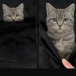 May include: A gray tabby cat peeking out of a black pocket. The cat's head is visible in the pocket on the left, and the cat is giving the middle finger in the pocket on the right.