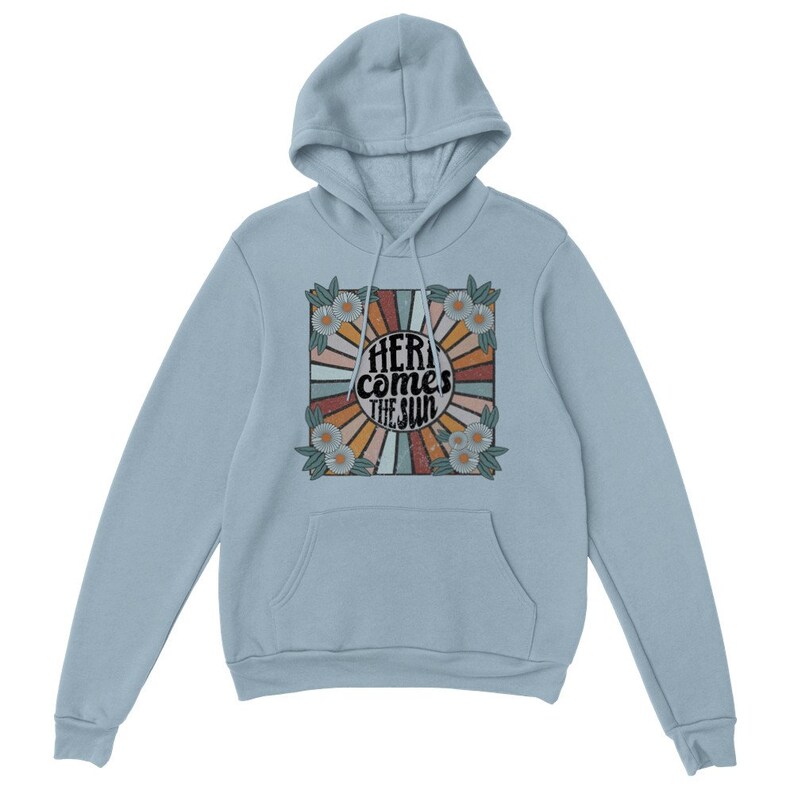 Op de afbeelding: Lichtblauwe hoodie met een retro-stijl grafische print van een zon met stralen en bloemen. De tekst "Here comes the sun" is in zwart op de print gedrukt.