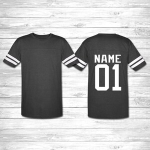 May include: A dark gray t-shirt with white stripes on the sleeves. The back of the shirt has the text "NAME 01" in white.