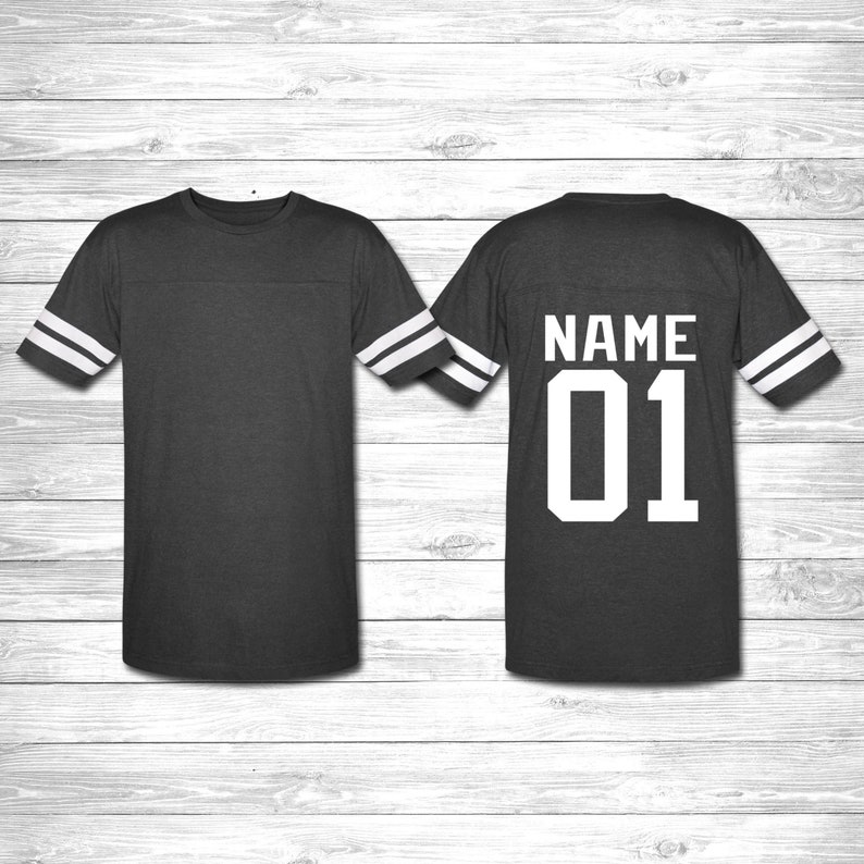 May include: A dark gray t-shirt with white stripes on the sleeves. The back of the shirt has the text "NAME 01" in white.
