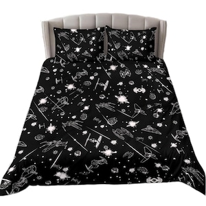 May include: A black and white bedding set with a space-themed pattern. The pattern features stars, planets, and spaceships. The bedding set includes a duvet cover and two pillowcases.
