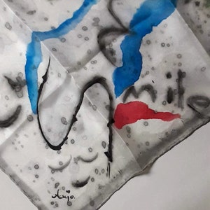 May include: A white silk scarf with abstract blue, red, and black watercolor designs. The scarf has a signature in the bottom left corner that says "Aujo."