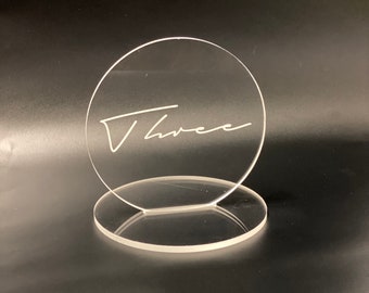 May include: Clear acrylic table number with the word "Three" written in white script.