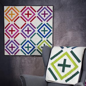 Könnte beinhalten: Zwei bunte Quilts mit einem geometrischen Muster aus weißen Quadraten mit einem Pluszeichen in der Mitte. Die Quilts sind aus verschiedenen Stoffen in den Farben Rot, Orange, Gelb, Grün, Blau, Lila und Weiß gefertigt. Die Quilts hängen an einer grauen Wand.