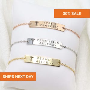 Op de afbeelding: Drie medische waarschuwingsarmbanden met schakelkettingen. De armbanden zijn goud, zilver en ros&eacute;goud. Elke armband heeft een rechthoekige plaat met een medisch symbool en de tekst: "TYPE 1 DIABETIC", "PENICILLIN ALLERGY" en "PEANUT ALLERGY".