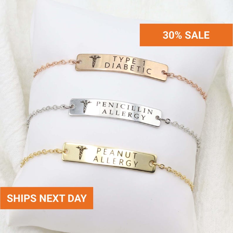 Op de afbeelding: Drie medische waarschuwingsarmbanden met schakelkettingen. De armbanden zijn goud, zilver en ros&eacute;goud. Elke armband heeft een rechthoekige plaat met een medisch symbool en de tekst: "TYPE 1 DIABETIC", "PENICILLIN ALLERGY" en "PEANUT ALLERGY".