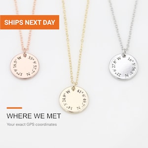 May include: Three necklaces with circular pendants in rose gold, yellow gold, and silver tones. Each pendant features engraved GPS coordinates. The text on the pendants includes numerical values followed by N and W. The necklaces have thin metal chains.
