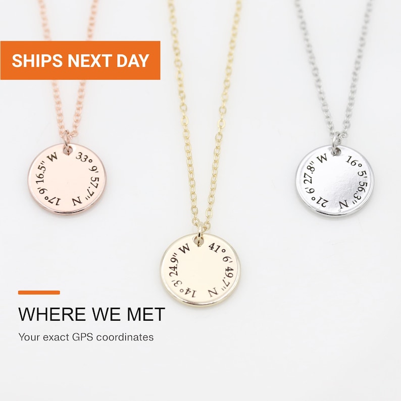 May include: Three necklaces with circular pendants in rose gold, yellow gold, and silver tones. Each pendant features engraved GPS coordinates. The text on the pendants includes numerical values followed by N and W. The necklaces have thin metal chains.