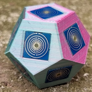 Peut inclure: Une forme géométrique imprimée en 3D avec un motif bleu et argent sur chaque face. La forme est peinte dans un schéma de couleurs bleu clair et rose.