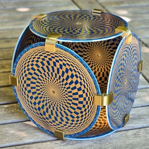 Puede incluir: Una escultura geométrica hecha de seis paneles circulares con un patrón de cuadros dorados y azules. Los paneles están conectados por soportes de metal dorado.