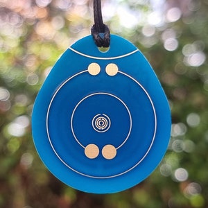 May include: A blue pendant necklace with a gold geometric design. The pendant features concentric circles and dots.