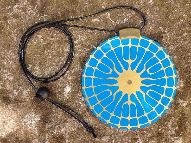 May include: A gold and blue pendant necklace with a geometric design. The pendant is round and has a gold center with a blue pattern.