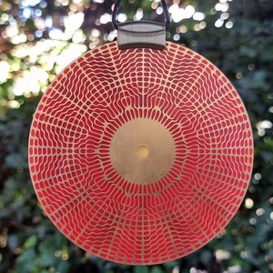 May include: A red and gold circular pendant with a geometric pattern. The pendant has a textured surface and a circular design in the center.