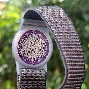 Può includere: Un braccialetto nero e argento con un design geometrico viola e oro. Il braccialetto è realizzato in tessuto intrecciato.