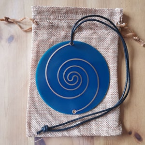 May include: A blue circular pendant with a gold spiral design, hanging from a black cord and resting in a burlap pouch.