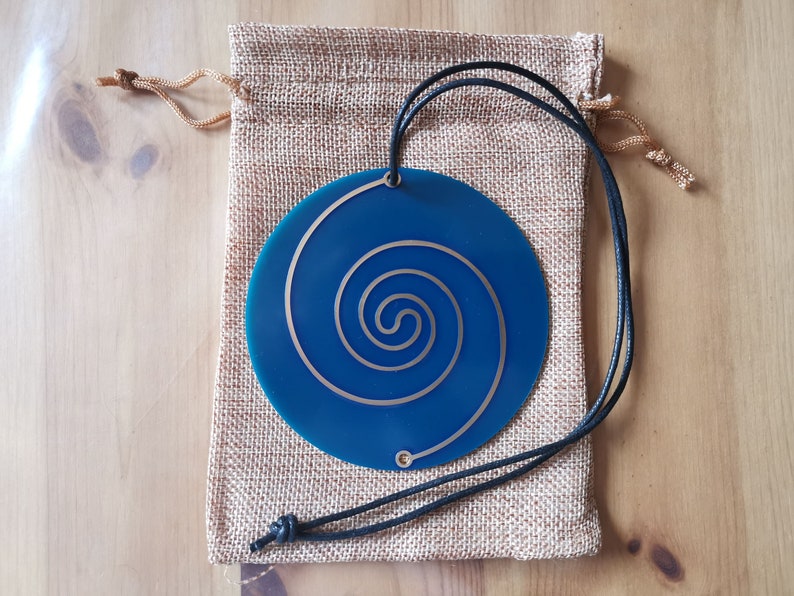 May include: A blue circular pendant with a gold spiral design, hanging from a black cord and resting in a burlap pouch.