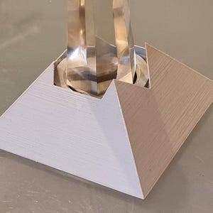 Peut inclure: Une base pyramidale blanche et beige avec une sculpture en verre transparent sur le dessus.