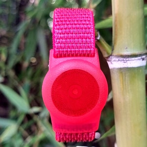 May include: A bright pink wristband with a round, red, light-up button. The button has a concentric circle pattern.