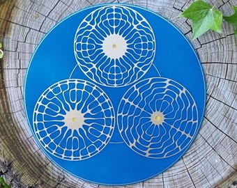 May include: A blue decorative piece featuring three white, circular designs with intricate patterns. The circles are arranged in a triangular formation. The piece is set against a natural wood background.