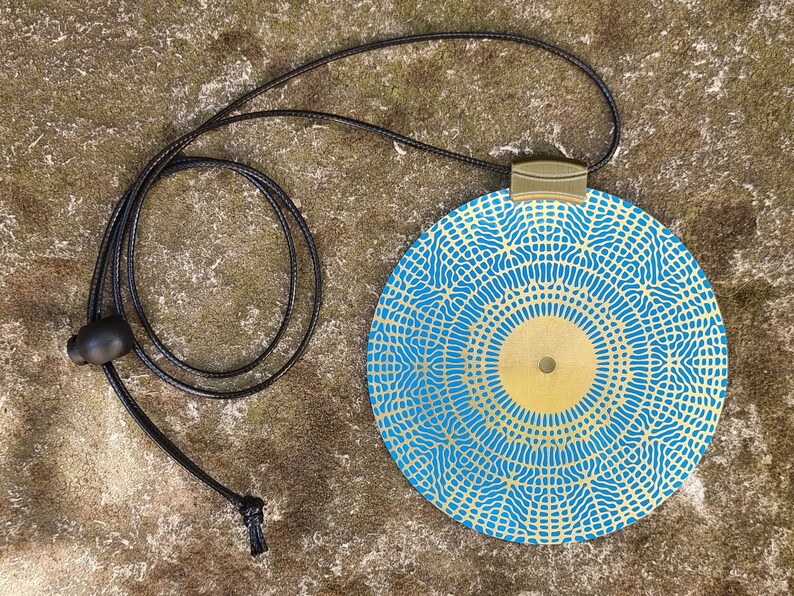 May include: A round blue and gold pendant necklace with a geometric pattern. The pendant is attached to a black cord.