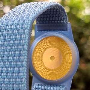 May include: A blue and white patterned wristband with a yellow circular sensor in the centre.