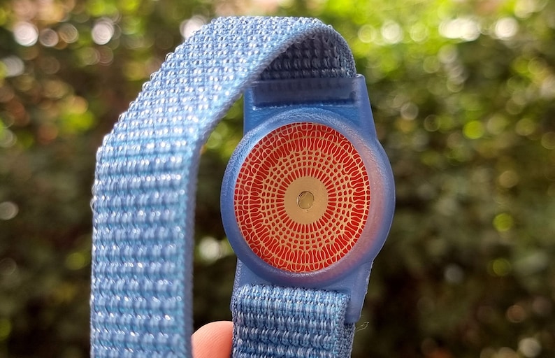 May include: A blue wristband with a red and silver circular tag. The tag has a geometric pattern.