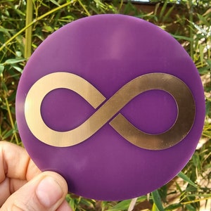 May include: A purple round disc with a gold infinity symbol in the center.