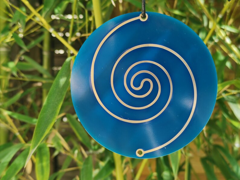May include: A blue circular pendant with a silver spiral design. The pendant is hanging from a black cord.