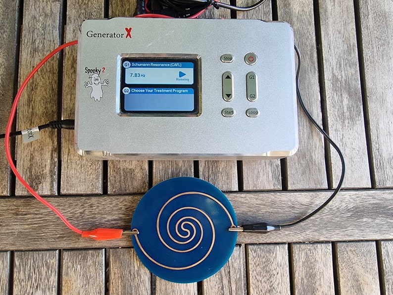 May include: A silver device labeled "Generator X" with a screen displaying "Spooky 2" and "Schumann Resonance (CAFL)" with a frequency of 7.83Hz. The device is connected to a blue circular coil with a copper spiral.