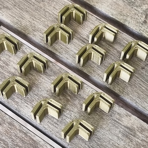 Puede incluir: Un conjunto de 14 soportes de esquina de plástico verde oliva. Los soportes están diseñados para conectar dos piezas de madera en un ángulo de 90 grados.