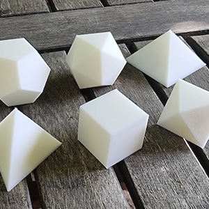 Peut inclure: Un ensemble de six formes géométriques blanches, comprenant un cube, une pyramide et un dodécaèdre. Les formes sont faites d'un matériau blanc lisse et sont disposées sur une surface en bois.