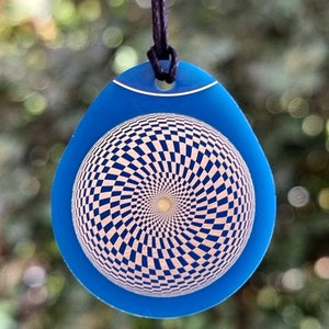 Peut inclure: Un pendentif bleu avec un motif en damier argenté, tourbillonnant à l'intérieur. Le pendentif a la forme d'une larme et est doté d'un cordon noir.
