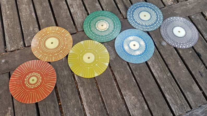 Puede incluir: Siete posavasos redondos con un patr&oacute;n geom&eacute;trico en tonos de rojo, naranja, amarillo, verde, azul y gris. Los posavasos tienen un centro dorado.