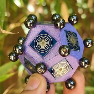 Pode incluir: Um objeto geométrico roxo com esferas pretas presas a cada ponto. O objeto tem um design azul e dourado em cada face.