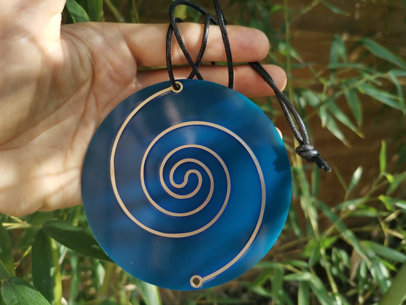 May include: A blue and gold spiral pendant necklace. The pendant is round and has a spiral design in gold on a blue background. The necklace is made of black cord.