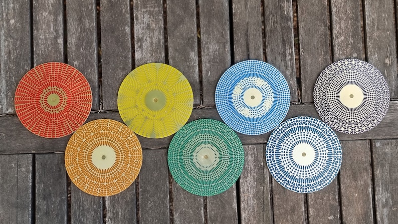 Puede incluir: Siete posavasos redondos decorativos con diferentes patrones geom&eacute;tricos en rojo, amarillo, azul, verde y negro. Los posavasos tienen un centro dorado.