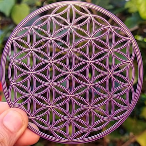 Könnte beinhalten: Ein violettes und goldenes Metall-Lebensblume-Mandala mit komplizierten geometrischen Mustern.