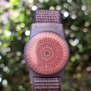 May include: A round, brown wristband with a circular, red and white patterned design in the center.
