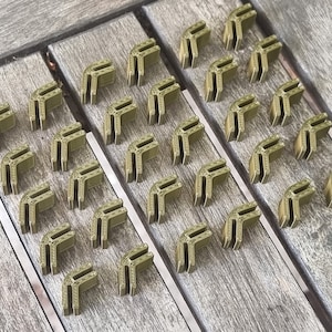 Puede incluir: Un conjunto de 30 piezas de esquina de plástico verde para proyectos de construcción o manualidades. Las piezas están dispuestas en filas sobre una superficie de madera.