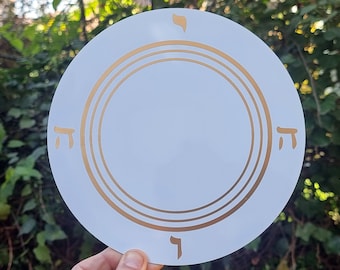 May include: White circular disc with concentric gold rings and Hebrew letters around the edge.