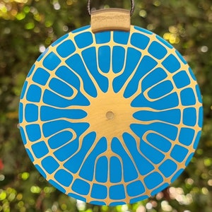 May include: A round, blue and gold pendant with a geometric pattern. The pendant is made of metal and has a shiny finish.