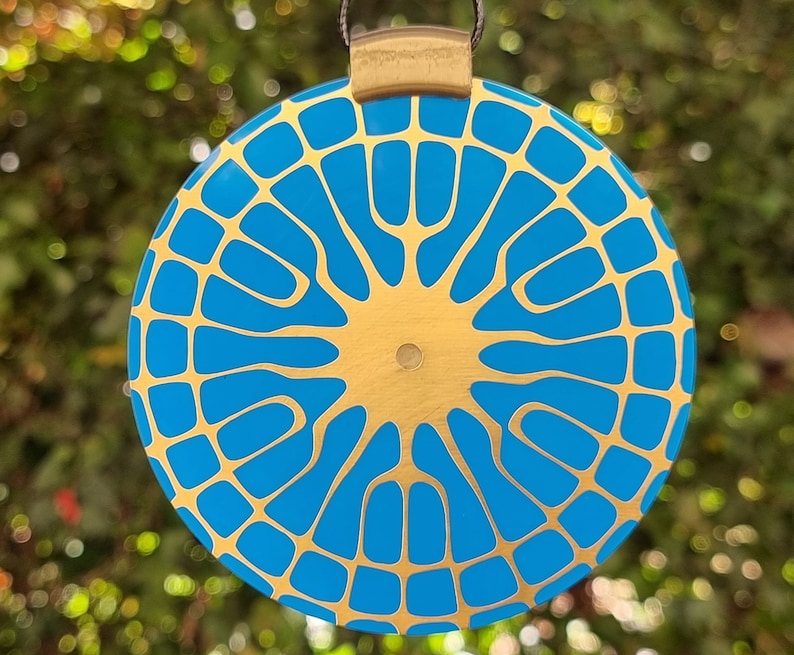 May include: A round, blue and gold pendant with a geometric pattern. The pendant is made of metal and has a shiny finish.