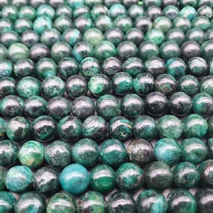 Peut inclure: Gros plan sur un brin de perles de pierres précieuses vert foncé. Les perles sont rondes et ont une finition lisse et polie.